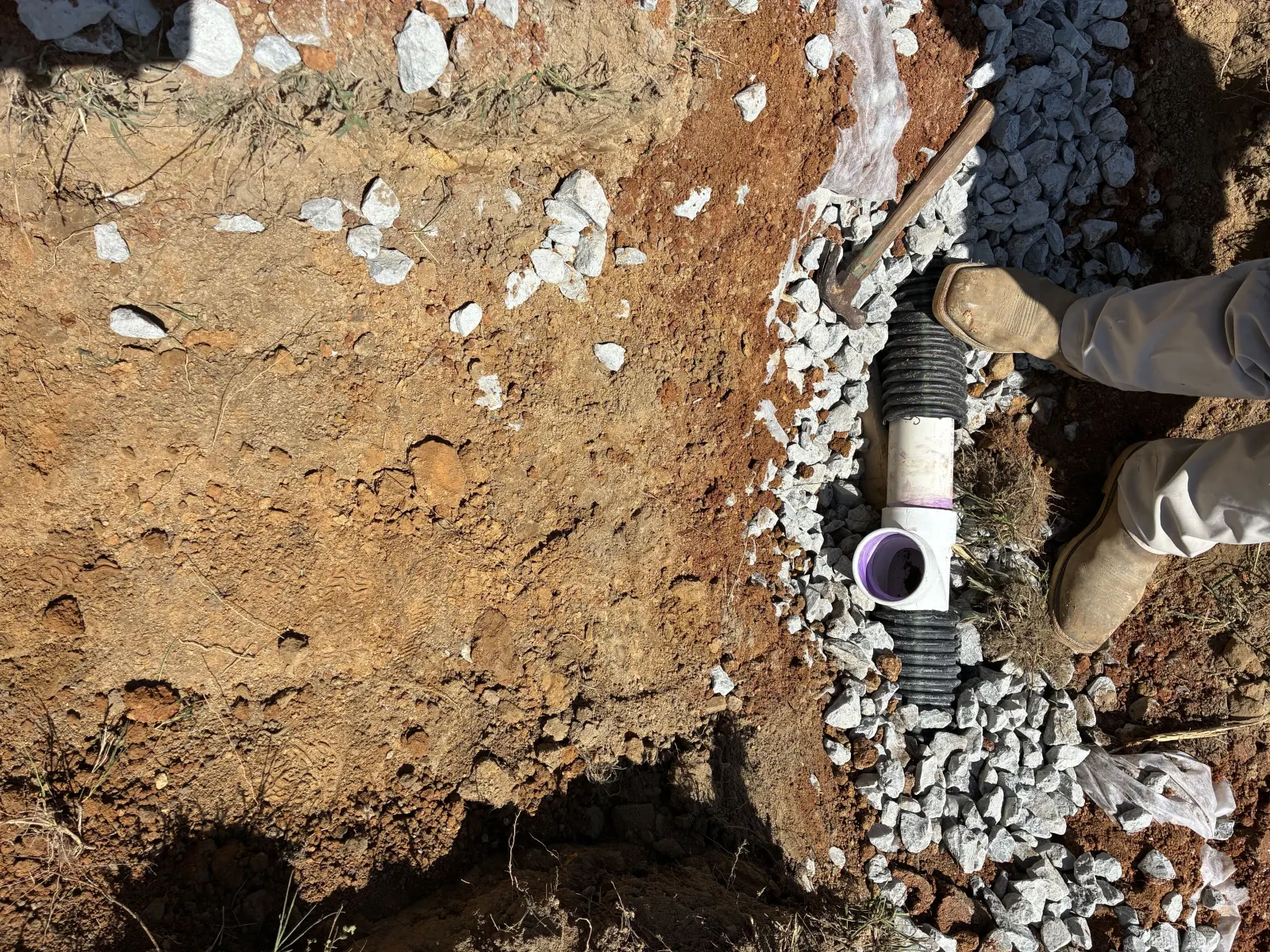 Perforated pipe being fitted into a gravel drain field trench