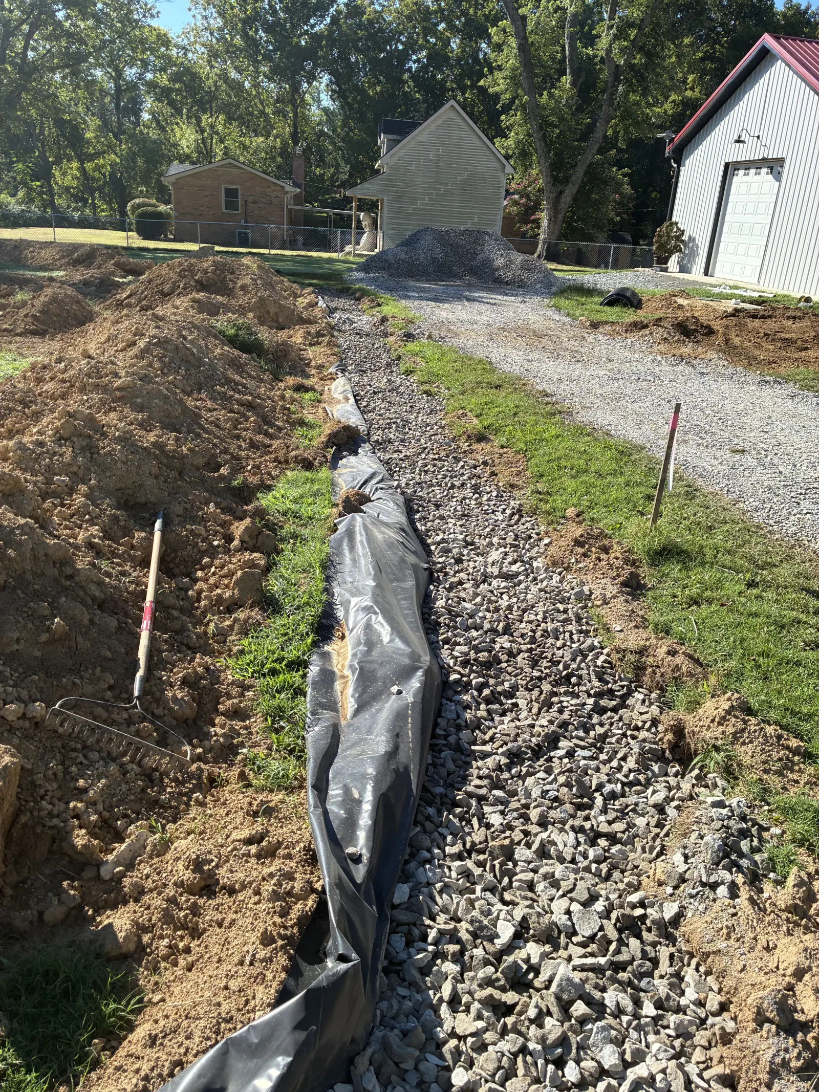 Drain field trench running along a gravel driveway toward a house