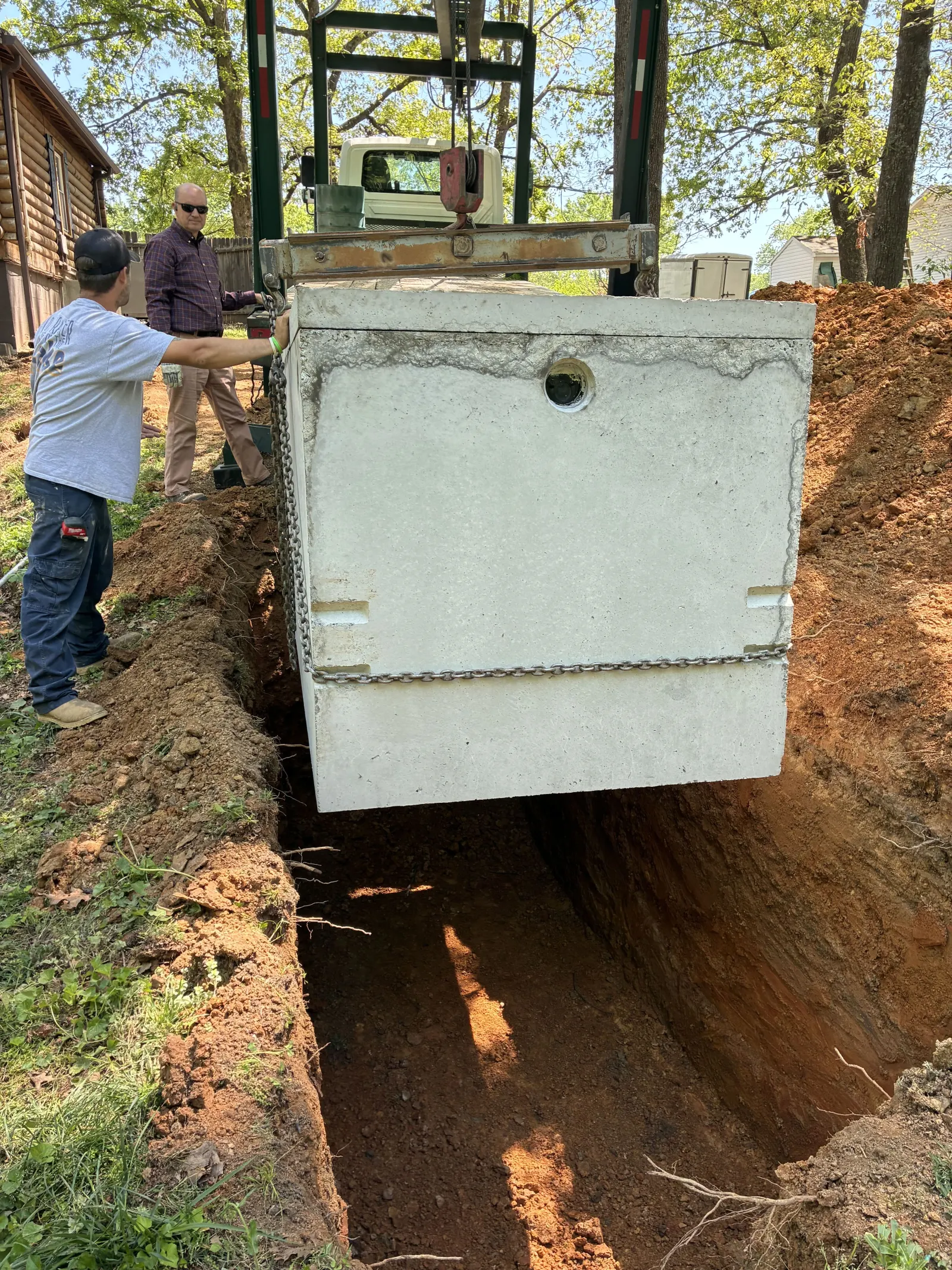 Crew guiding a precast septic tank into the hole