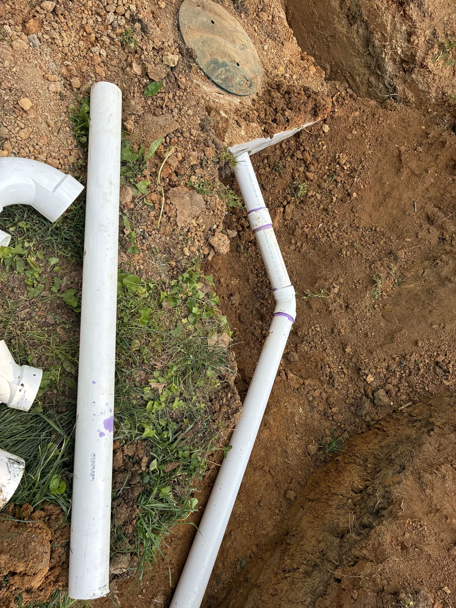 Pipe and elbow fittings set in the trench beside a tank lid